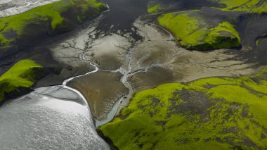 İzlanda 'nın yeşil yosunlarının hava perspektifi tepeleri, karanlık volkanik arazileri, örülmüş nehirleri ve yansıtıcı su kütlesinin yanındaki küçük kırmızı yapıyı kapsıyor..