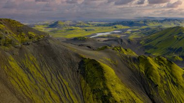 İzlanda 'nın engebeli volkanik arazisinin hava perspektifi yeşil yosun, karanlık toprak, dolambaçlı nehirler ve bulutlu bir gökyüzü altında dağılmış göller..