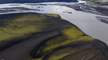 İzlanda 'nın volkanik arazisinin koyu kül, yeşil yosun ve çarpıcı zıtlıklar ve dokular yaratan gümüş kıvrımlı bir nehir görüntüsü..