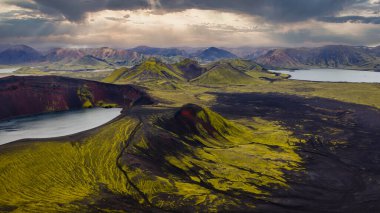 Volkanik kraterleri, karanlık lav tarlalarını ve İzlanda 'nın dağlık bölgelerindeki bulutlu gökyüzünün altındaki dingin gölleri kaplayan yosun manzarası..