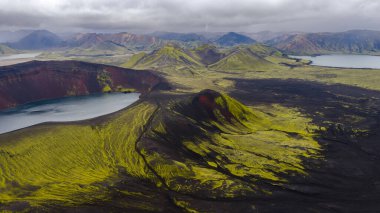 Bir krater gölü, engebeli toprak, yeşil yosun, çok renkli dağlar ve bulutlu bir gökyüzü içeren İzlanda 'nın volkanik arazisinin hava perspektifi..
