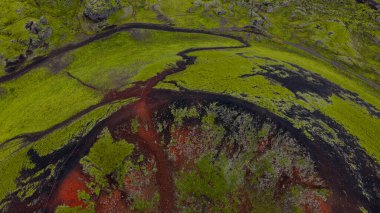 İzlanda 'daki bir volkanik kraterin hava görüntüsü, kırmızı ve siyah toprak, yemyeşil yosun, kıvrımlı kenarlar ve canlı zıtlıklarla dolu engebeli arazi..