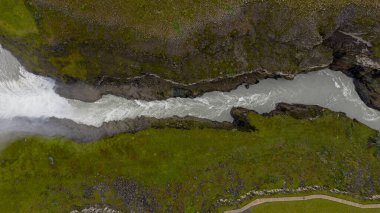 İzlanda 'da yosun kaplı kayalıkları olan derin bir vadiden bir buzul nehri akar. Tırabzanlı bir yürüyüş yolu görülebilir, turist girişini vurguluyor.