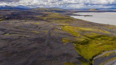 Yeşil yosun, dolambaçlı yol, elektrik hatları, göl, tepeler ve bulutların altındaki uzak dağlar ile İzlanda 'nın volkanik arazisinin hava perspektifi..