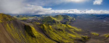 İzlanda 'nın engebeli volkanik arazisinin hava perspektifi, bulutlu bir gökyüzünün altında yeşil yosun kaplı dağlar, karanlık toprak, çıkıntılar ve vadilerin yer aldığı.