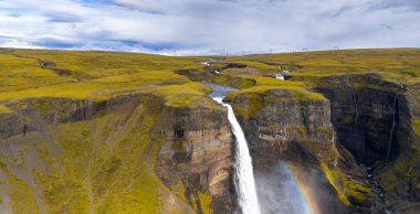 Güçlü bir şelale İzlanda 'da volkanik kayalıklarla çevrili bir kanyona düşer. Sisin içinde bir gökkuşağı beliriyor, elektrik hatları görünür..