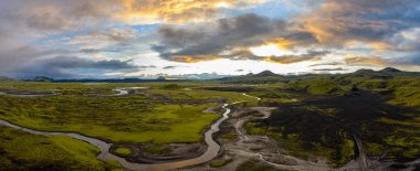 İzlanda 'nın dolambaçlı nehirleri, yeşil yosun kaplı arazi ve gün batımında tepeler ve dağlar tarafından çerçevelenmiş karanlık volkanik toprak perspektifi..