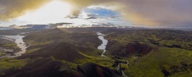 Sarmal bir nehir yeşil vadiler ve volkanik araziler boyunca akar, krater oluşumları, sakin bir göl, ve İzlanda 'nın manzarasında altın bir gökyüzü.