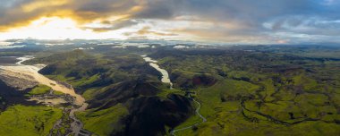 Sarmal bir nehir, İzlanda 'daki yemyeşil vadilerden ve volkanik tepelerden akar. Engebeli oluşumları ve manzarayı aydınlatan altın bir günbatımı vardır..