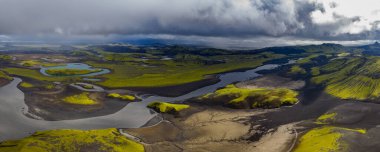 Sarmal nehirler, siyah kumlar, yeşil yosun kaplı tepeler, küçük göller ve uzak dağlarla İzlanda 'nın volkanik arazisinin hava perspektifi.