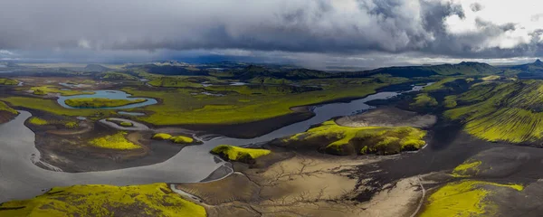 Sarmal nehirler, siyah kumlar, yeşil yosun kaplı tepeler, küçük göller ve uzak dağlarla İzlanda 'nın volkanik arazisinin hava perspektifi.