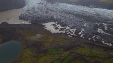 Drone buz desenleri, eriyen su akıntıları, yosunlu bitki örtüsü, volkanik toprak ve soldaki küçük gölle İzlanda 'nın buzullarında ilerler..