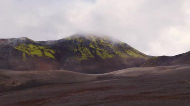 Drone İzlanda 'da volkanik bir dağ yakalar yeşil yosun çizgileri, karanlık toprak ve sis kaplı zirve, engebeli araziyi ve zıtlıkları gözler önüne serer.