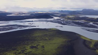 Yeşil yosun, kıvrımlı nehirler ve soluk bir gökkuşağı ile İzlanda 'nın volkanik manzarasının havadan görüntüsü. İnsansız hava aracı dağları ve su kaynaklarını aşıyor..