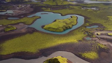 Turkuaz bir göldeki yeşil yosunların hava manzarası. Etrafı karanlık volkanik toprak ve İzlanda 'nın arazisindeki daha küçük su kütleleriyle çevrili..