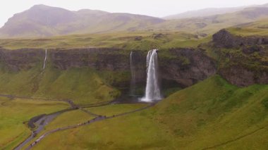 İzlanda 'daki Seljalandsfoss şelalesinin havuz manzarası. Bereketli yeşil alanlar, yürüyüş yolları ve uzak şelaleler görülebilir..