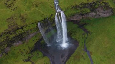 İzlanda 'daki Seljalandsfoss şelalesinin hava manzarası, suyun bir havuza, dolambaçlı bir nehre ve yakınlardaki yürüyüş yollarındaki insanları gösteriyor..