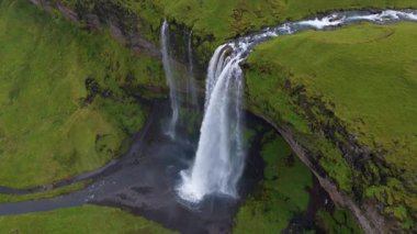 İzlanda 'daki Seljalandsfoss şelalesinin hava manzarası güçlü akışını, yemyeşil arazisini, dolambaçlı nehrini ve karanlık kaya oluşumlarını gösteriyor..