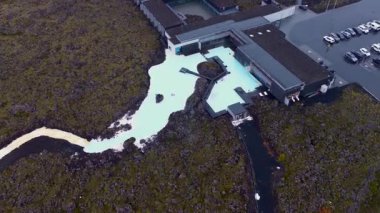 İzlanda 'daki Mavi Göl Jeotermal Kaplıcaları' nda pürüzsüz bir insansız hava aracı uçuşu. Süt mavisi suları, lav alanları, modern mimari ve dolambaçlı yolları gösteriyor..