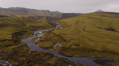 Yosun kaplı tepeler, vadiler ve İzlanda 'nın volkanik arazisindeki dar yolları olan engebeli dağlardan geçen dolambaçlı bir nehrin havadan görünüşünü süpürüyor..