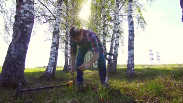 Een mens schat jager in een shirt met een metaaldetector opgegraven van een munt en is blij — Stockvideo