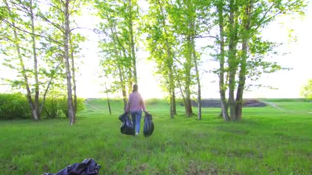 Εθελοντής με πλαστικές σακούλες με σκουπίδια στα χέρια του το κορίτσι είναι στο πάρκο — Αρχείο Βίντεο