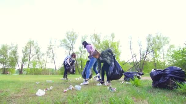 Teenager-Mädchen und Freiwillige sammeln Müll in Plastiktüten im sonnigen Park — Stockvideo