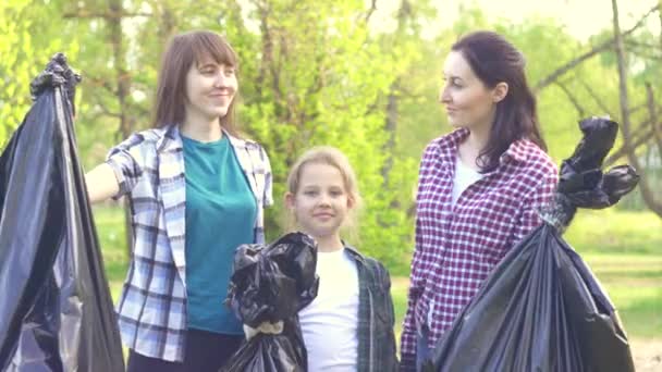 Retrato de dos voluntarias y una adolescente en camisas con bolsas de plástico con basura en las manos — Vídeos de Stock