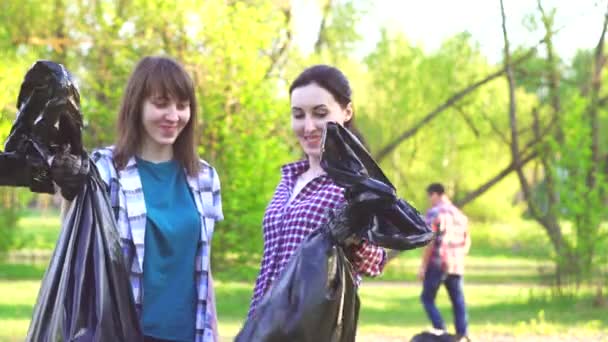 Портрет двух молодых девушек в футболках с пластиковыми пакетами с мусором в руках, смотрящих в камеру — стоковое видео