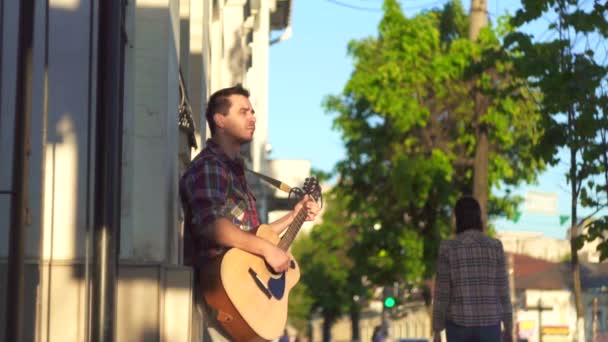 Уличный музыкант в футболке, играющий на гитаре на закате — стоковое видео