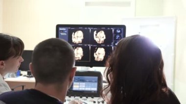 Doktor ve hamile bir kadın kocasıyla ultrason ekrana bakarak