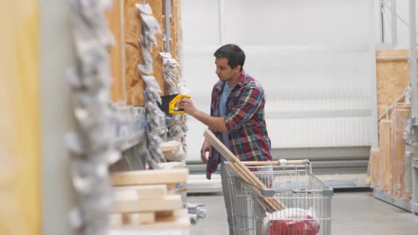 Человек в рубашке в хозяйственном магазине с тележкой покупает пилу — стоковое видео
