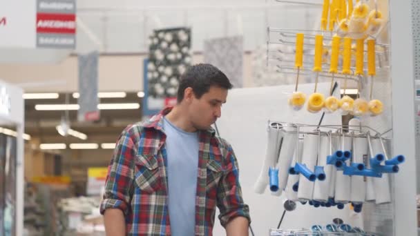 Мужчина 30 лет в клетчатой рубашке в хозяйственном магазине выбирает роллер для покраски — стоковое видео