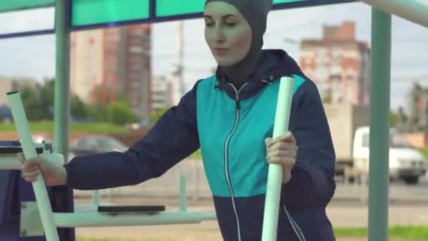 Uma menina em um hijab em um ginásio de rua no fundo da cidade e carros — Vídeo de Stock