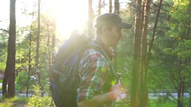 Чоловік турист у плетеній сорочці, що йде в парку з великим сонячним спалахом рюкзака — стокове відео