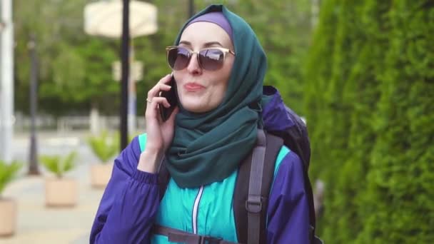 Porträtt av flicka turist i huvudduk och solglasögon i en ryggsäck som pratar i telefon — Stockvideo