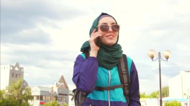 bir kız turistik bir başörtüsü ve telefonda konuşurken bir sırt çantası içinde güneş gözlüğü