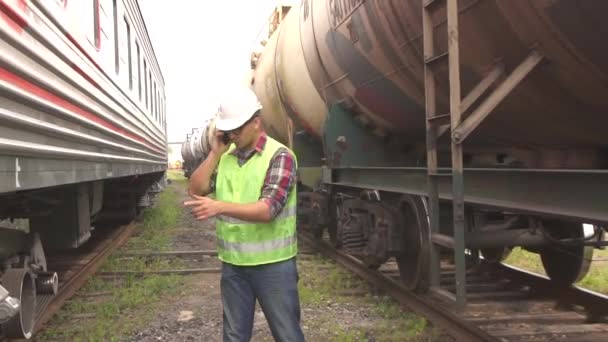 Muž v brýle pracovník kontroly vlaku v helmě a uniformu, chůze na nádraží mluvil po telefonu — Stock video