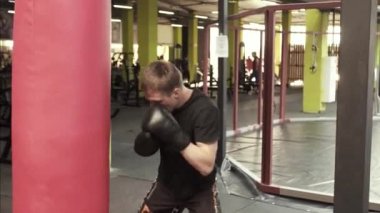 Genç boksör adam kum torbasına spor salonunda atıyor.