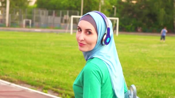 Attraktiva sportig muslimsk flicka i hijab går runt arenan och ler mot kameran, långsamma mo — Stockvideo