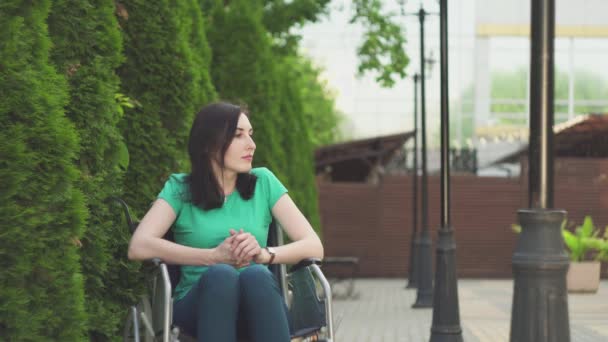 Χαριτωμένο κορίτσι με ειδικές ανάγκες σε μια αναπηρική καρέκλα, περιμένει το φίλο της στο πάρκο — Αρχείο Βίντεο