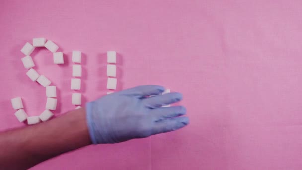 Word sugar is laid out by refined sugar cubes on a pink background. Concept of caries — Stock Video
