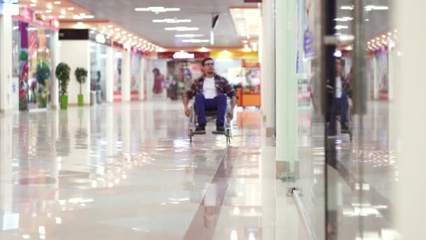 Человек с инвалидностью в инвалидной коляске едет в торговый центр и смотрит в окна — стоковое видео