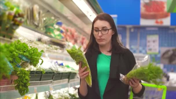 Porträtt attraktiva flicka med står inför ett val om vad man ska köpa i departementet med grönsaker i snabbköpet — Stockvideo