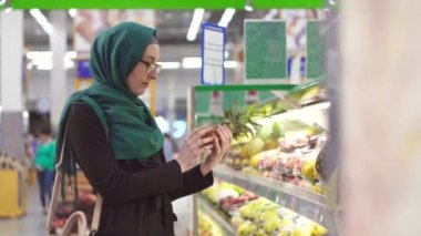 Müslüman kız hijab süpermarkette bir ananas seçer