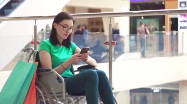 Tekerlekli sandalyede bir özürü olan bir kadın telefon alışveriş merkezinde alışveriş sonra kullanır. Yakın çekim