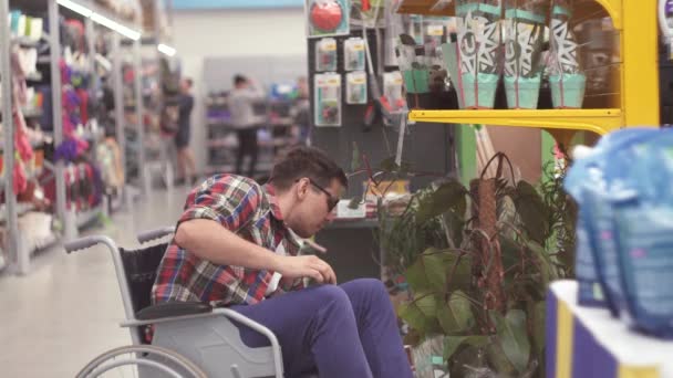 Homem vendedor com uma deficiência em uma cadeira de rodas coloca a mercadoria nas prateleiras na loja — Vídeo de Stock