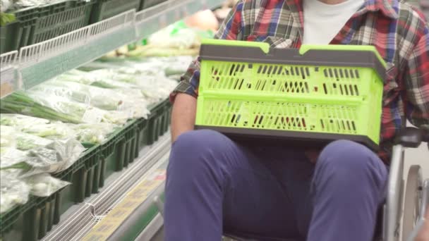 Uomo con disabilità in sedia a rotelle che fa shopping al supermercato.Ha un cesto di cibo sulle ginocchia. — Video Stock