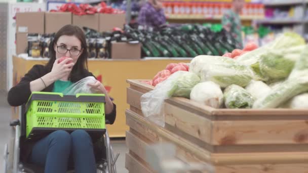 Ανάπηρη γυναίκα σε μια αναπηρική καρέκλα ψώνια στην υπεραγορά επιλέγει τις ντομάτες και τα βάζει σε ένα πακέτο. — Αρχείο Βίντεο