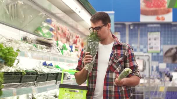 一个戴着眼镜的男人和一件带篮子的衬衣面临着在超市里买什么菜的选择 — 图库视频影像